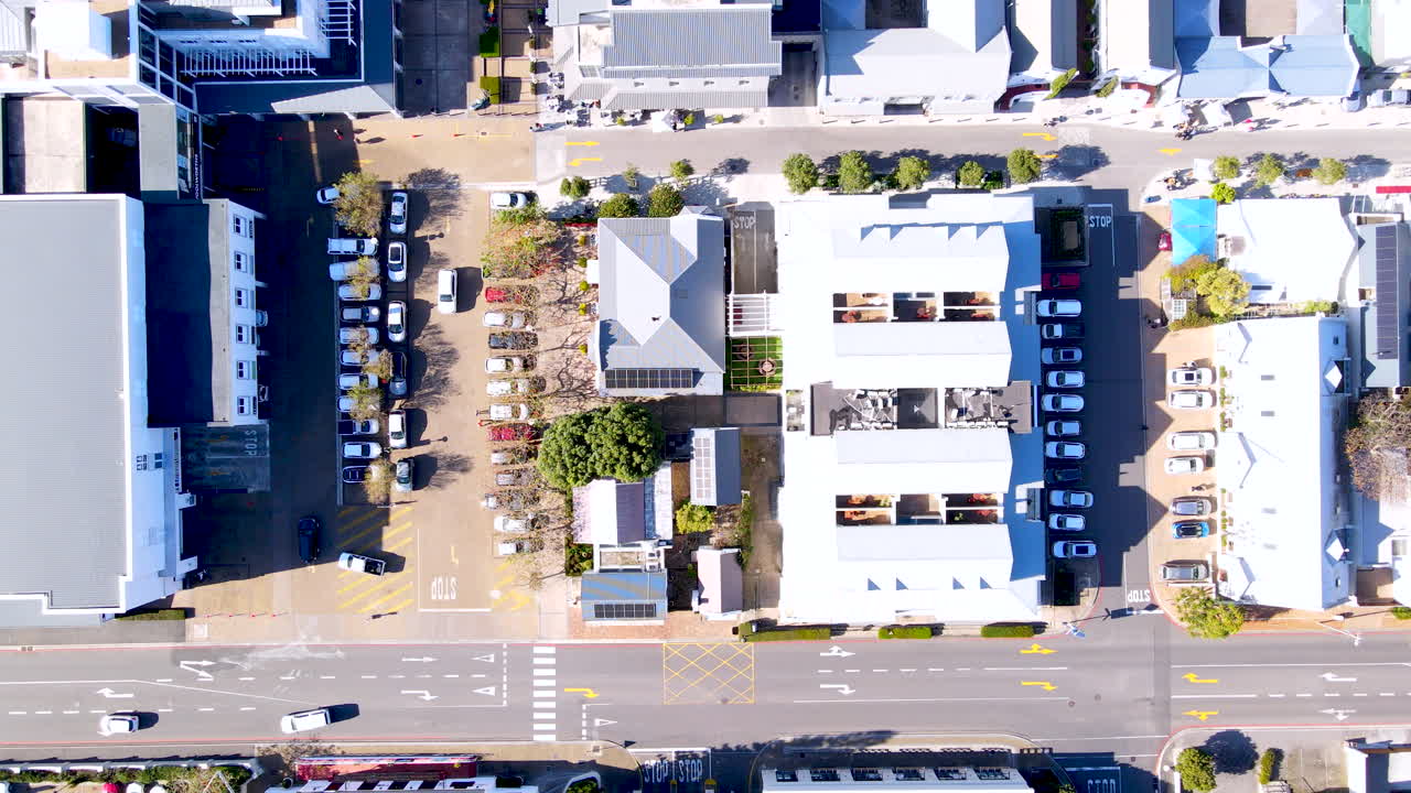 Top down aerial view over Hermanus CBD buildings as cars pull out from parking