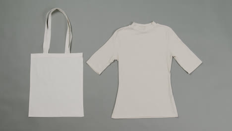 close up of white bag and t-shirt on grey background, with copy space, slow motion