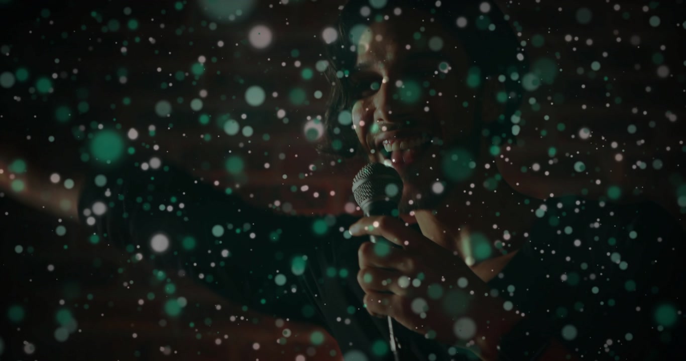 Floating bokeh drifting aside, male singer shifting forward, lifting mic and performing song