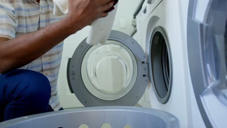 side view of mid adult black man washing clothes in washing machine at comfortable home 4k