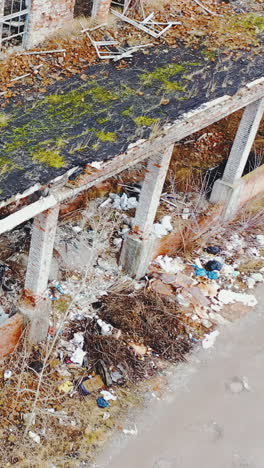 heaps of garbage, destroyed industrial buildings with collapsed roofs. grass and moss on the ruins. aerial close-up view. vertical video