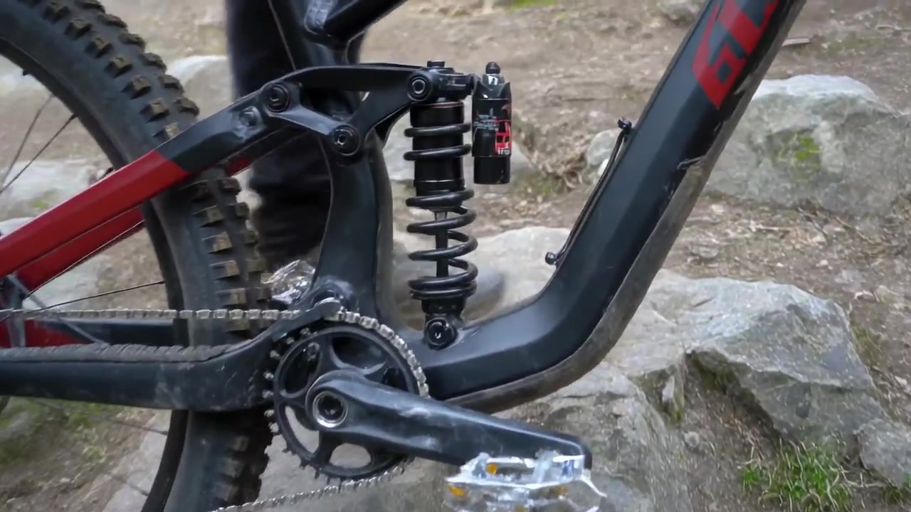 Telecamera di tracciamento che filma una ruota di bicicletta che rotola su radici su un sentiero nel bosco, mostrando l'ammortizzatore posteriore, con il ciclista che indossa stivali.