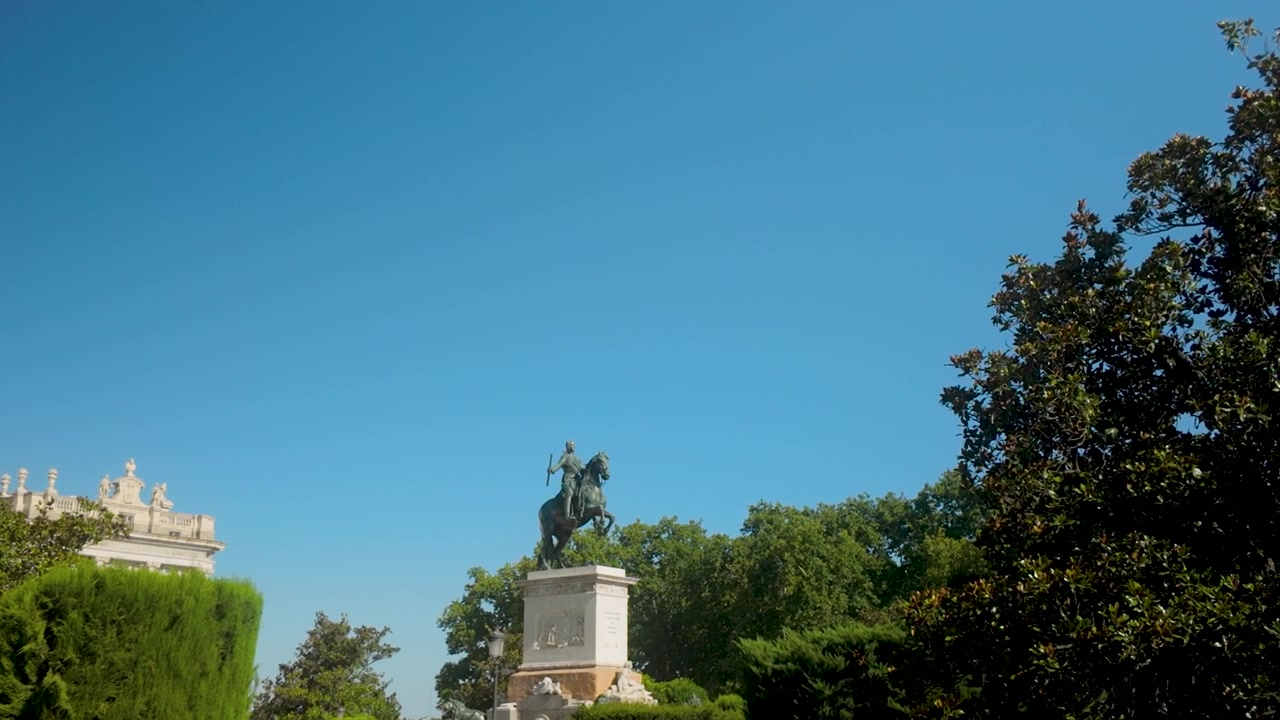 Una ripresa dal basso della storica statua equestre in bronzo di Re Filippo IV circondata da lussureggianti alberi verdi sotto un cielo azzurro limpido a Madrid.