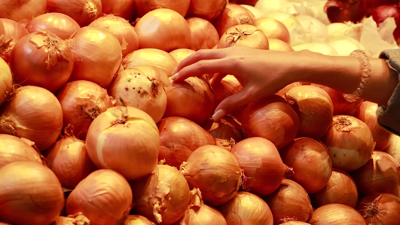A person examines and selects yellow onions from a supermarket pile under warm lighting