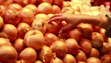 a person examines and selects yellow onions from a supermarket pile under warm lighting