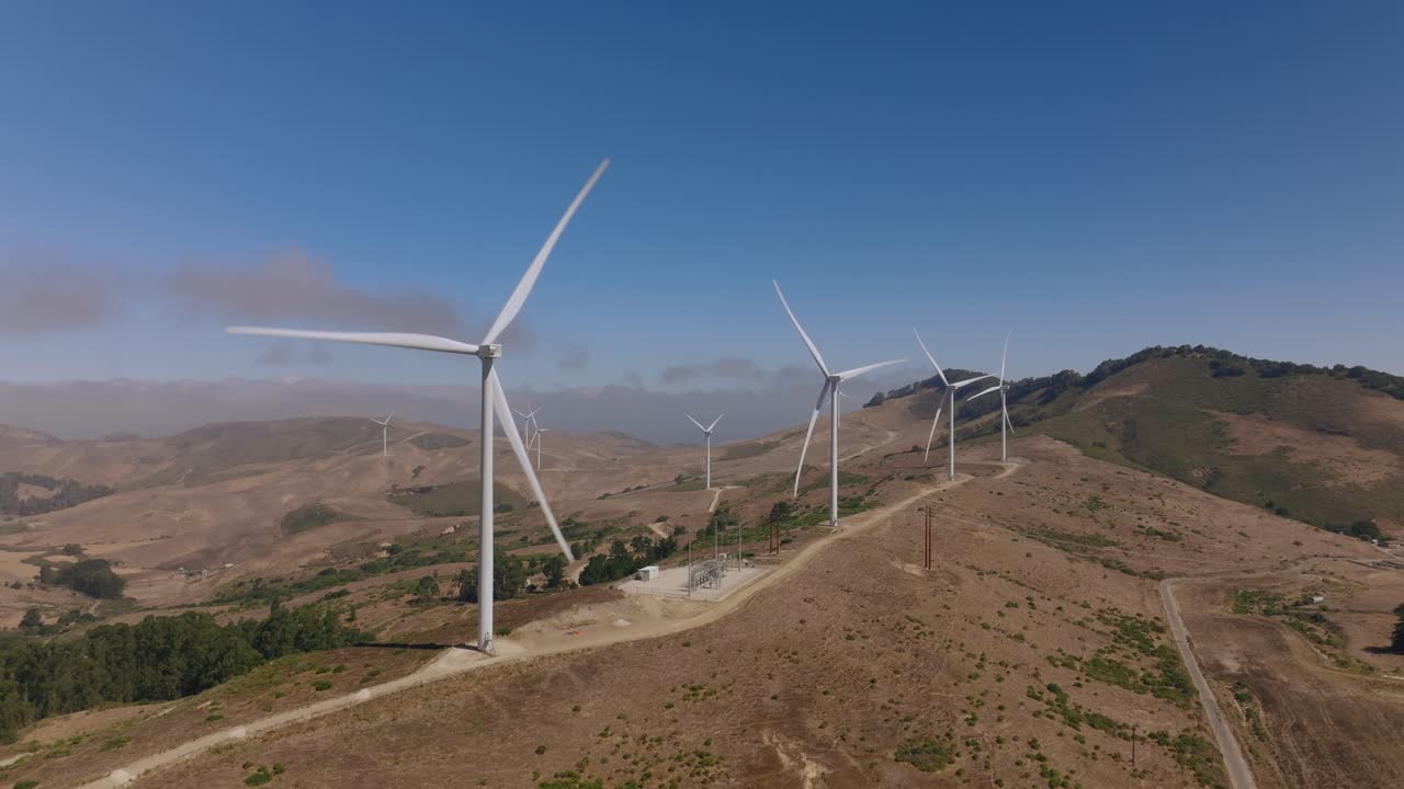Wind turbines spin on California hills under a clear blue sky