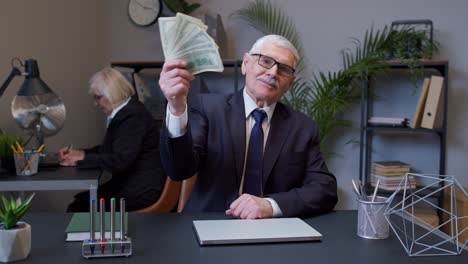 sonriente hombre de negocios de alto nivel agitando con una pila de dinero en el lugar de trabajo de la oficina después del éxito trabajo en línea
