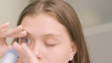 the young girl instill eye drops before installing night time contact lenses in an ophthalmologist's office. eyedropper putting liquid into open eye. child's eye drops.