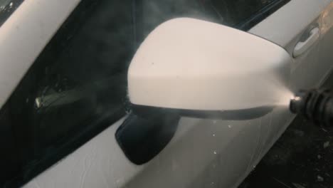 male cleaning a white car with a pressure washer