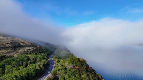 Aerial view of a mist-covered lake, winding road, and lush greenery under a clear blue sky