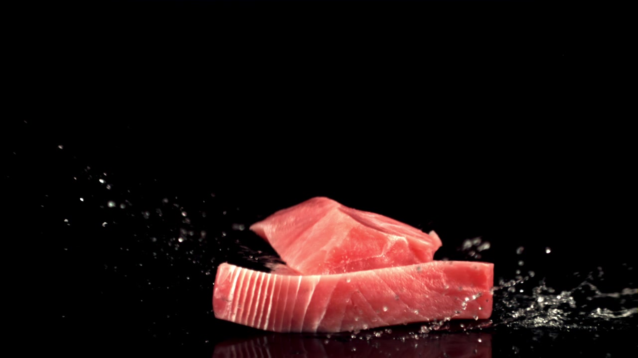 Bistecche di tonno fresco crudo che cadono e schizzano su sfondo nero