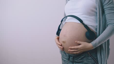 una joven embarazada pone auriculares en el vientre cerca de la pared