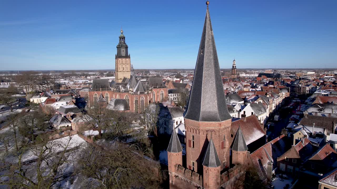 Aerial approach and passing of Drogenapstoren in tower town Zutphen towards Walburgiskerk cathedral with small historic Dutch city covered in snow in The Netherlands and river IJssel passing by behind
