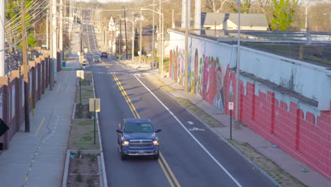 Static-Daytime-Morning-City-Streets-with-cars-driving-into-frame-Graffiti-on-wall-as-cars-drive-past-Morning-commuters-heading-to-work