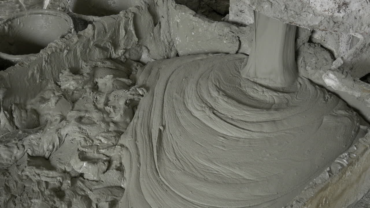 Cement mixer pouring mixed mortar in a huge box container as a contruction worker is shovelling them in individual pails
