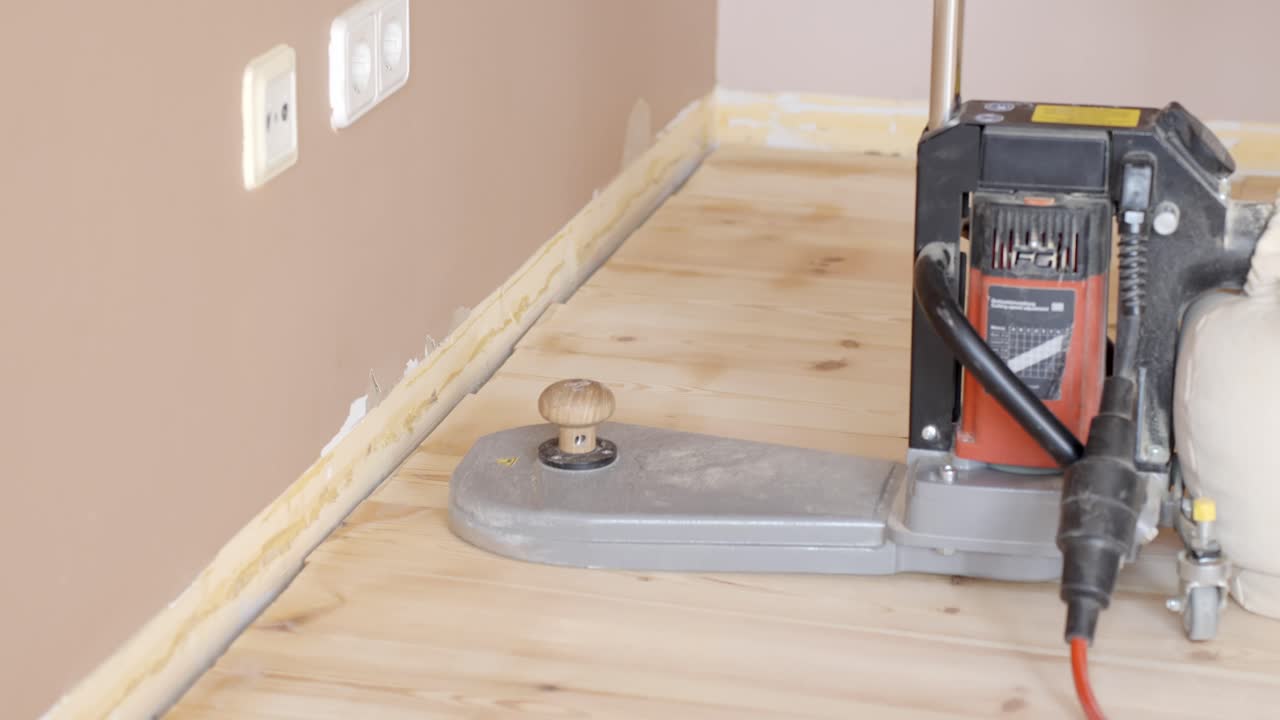 Power sander along wood floor edge to finish trim near the wall, balancing and sanding, closeup static