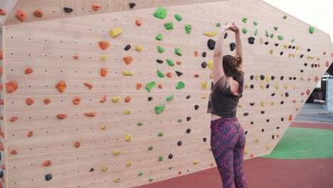 cinematic shot of a woman stretching in front of a climbing wall outside, slow motion, close up, moving shot