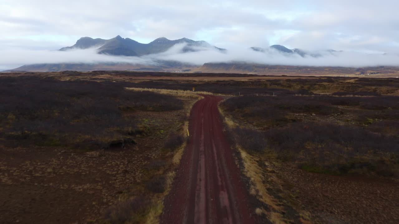 vuelo de drones sobre camino de tierra en el salvaje paisaje islandés, vista de montañas nubladas