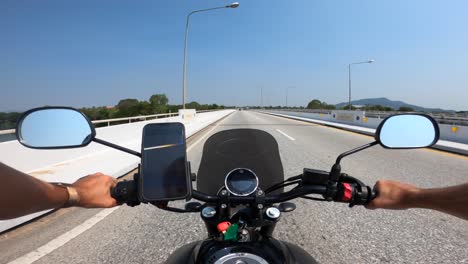 punto de vista hombre caucásico conduciendo una motocicleta yamaha en una carretera vacía en tailandia mientras los camiones conducen en la dirección opuesta en un día soleado con un iphone montado en la bicicleta