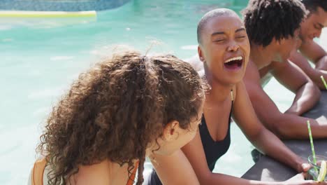 two diverse female friends with drinks laughing in swimming pool