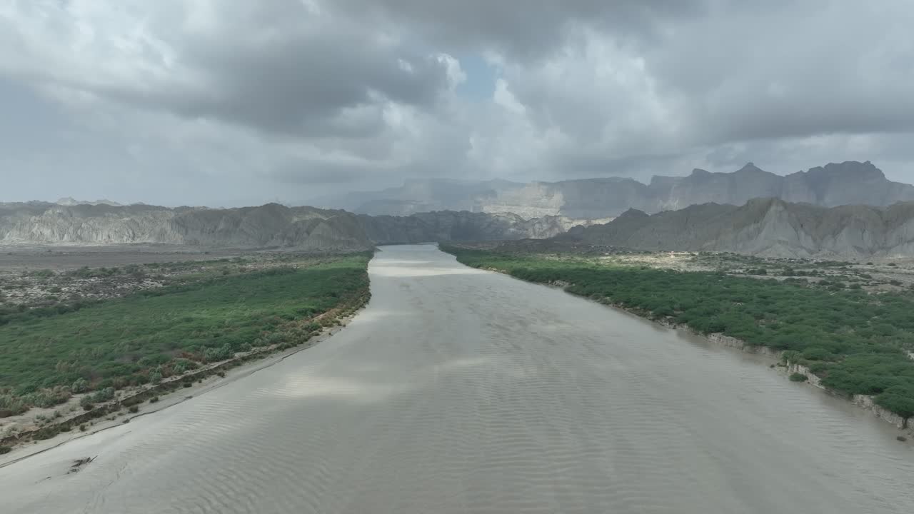 공중 무인기 (drone) 는 힌골 (hingol), 발로치스탄 (balochistan), 파키스탄의 백그라운드에서 산맥과 함께 초록색 식물로 둘러싸인 건조한 강바닥 위에서 찍은 사진입니다.