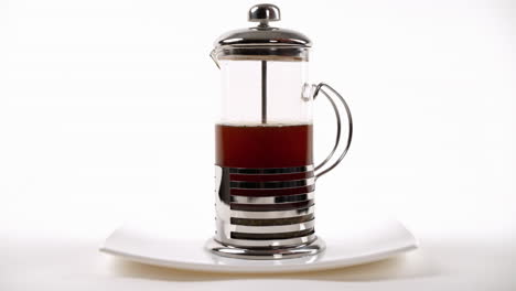 tea infusion in a french press on white plate, with plunger pressed halfway