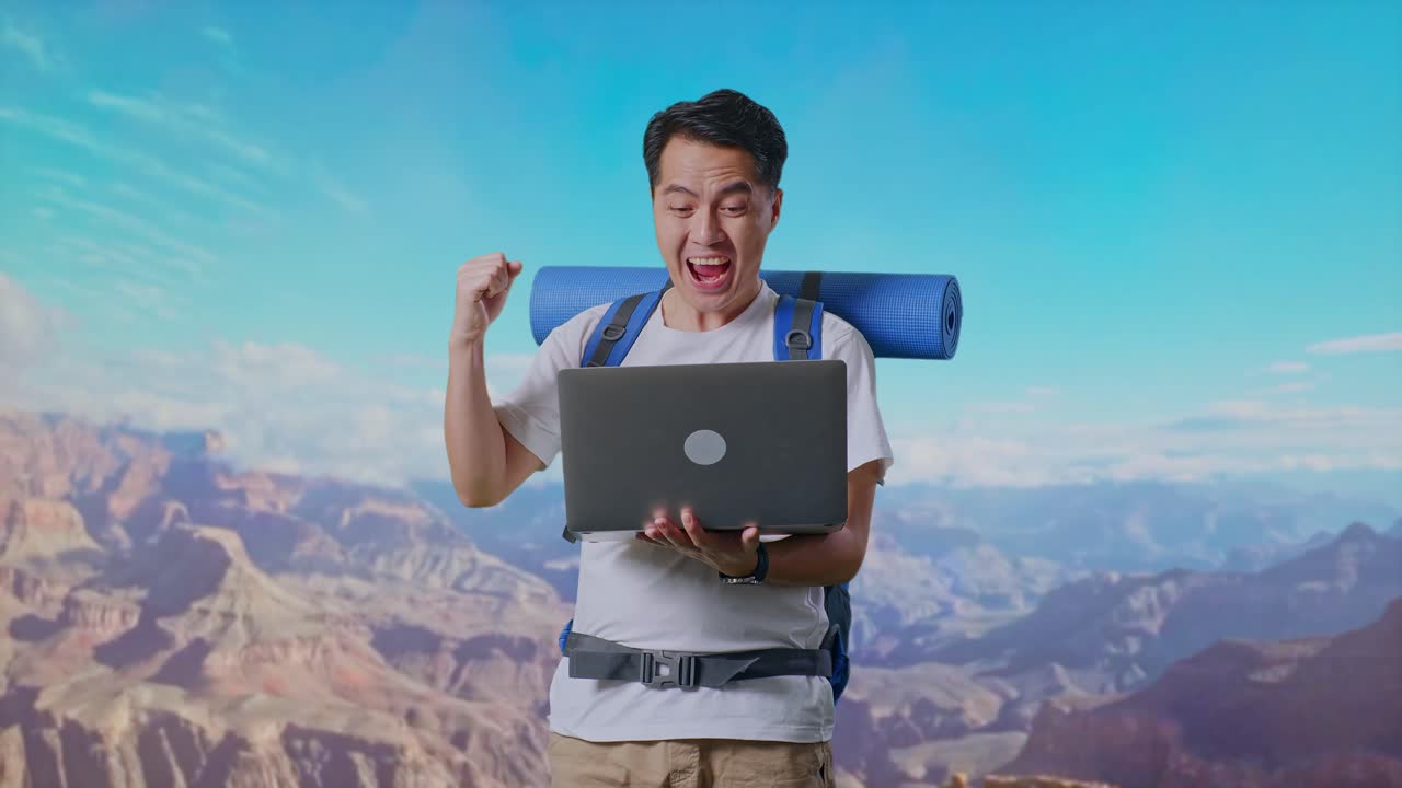 Asian Male Hiker With Mountaineering Backpack Looking At A Laptop And Screaming Goal Celebrating The Success While Traveling At The Top Of Mountain