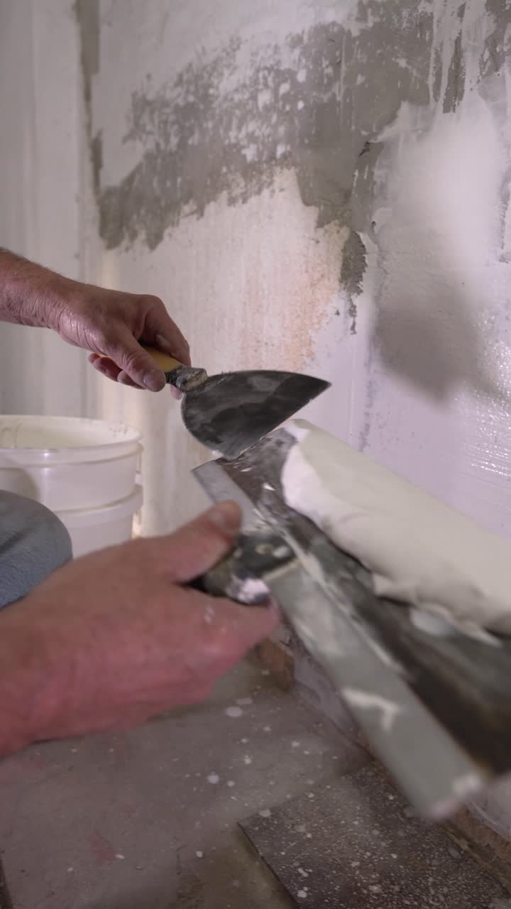 Close-up of hands preparing thick white putty or joint compound for wall surface repair and finishing using a wide metal trowel