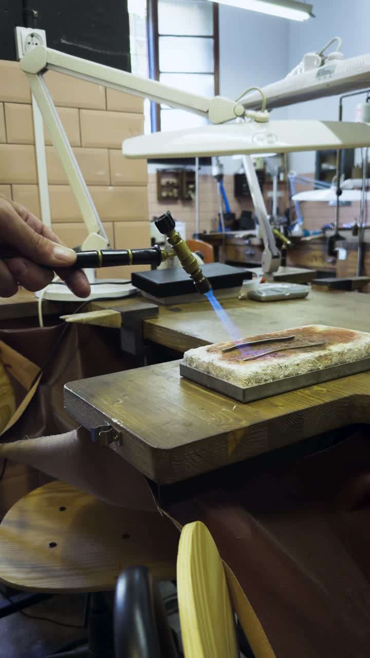 Handheld close-up of silver heating over flame in workshop, bending for handmade ring crafting
