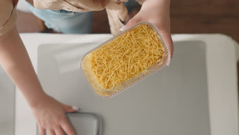 woman shakes transparent container with yellow spaghetti