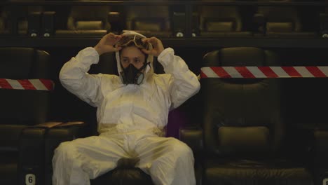 portrait of a man in white protection costume and respirator sitting alone at the cinema then remove it