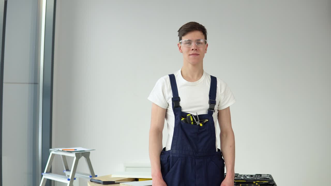 Young master in work uniform and with a set of tools stands on a white wall background