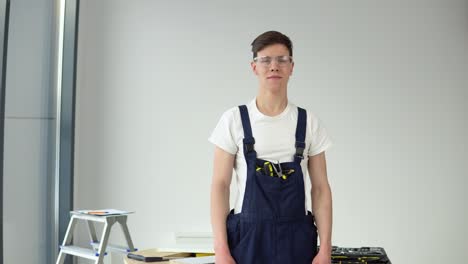 young master in work uniform and with a set of tools stands on a white wall background