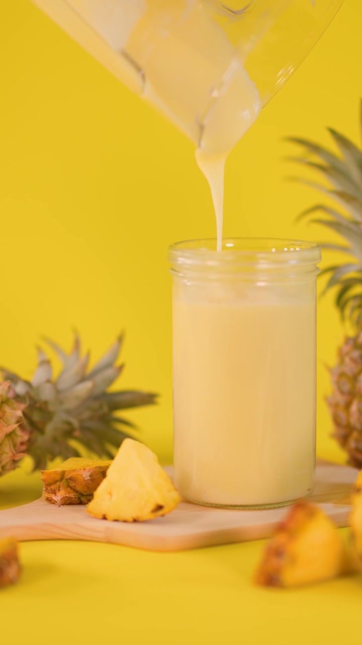 Versamento di frullato fresco all'ananas in un barattolo di vetro.