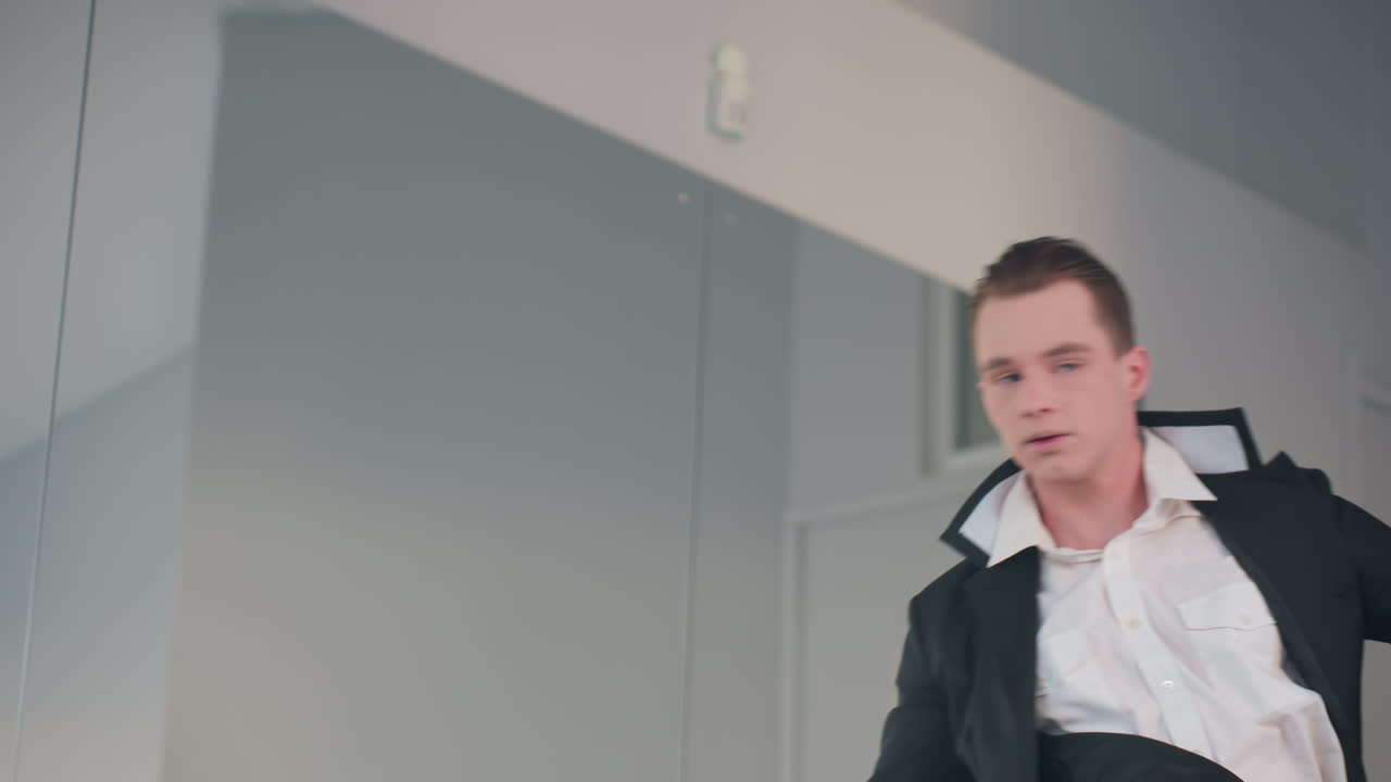 young man in black coat and white shirt stands pointe in ballet pose, confident posture facing away from camera, minimalist studio backdrop with soft natural light and mirror reflection