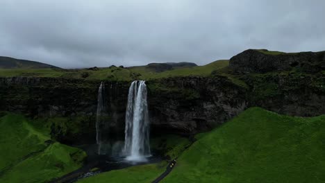 Luftaufnahme-Vom-Wasserfall-Seljalandsfoss,-Der-Vollständig-Umschlossen-Werden-Kann,-Umgeben-Von-Grüner-Landschaft-In-Island-Im-Sommer-Mit-Einem-Gefälle-Von-60-Metern