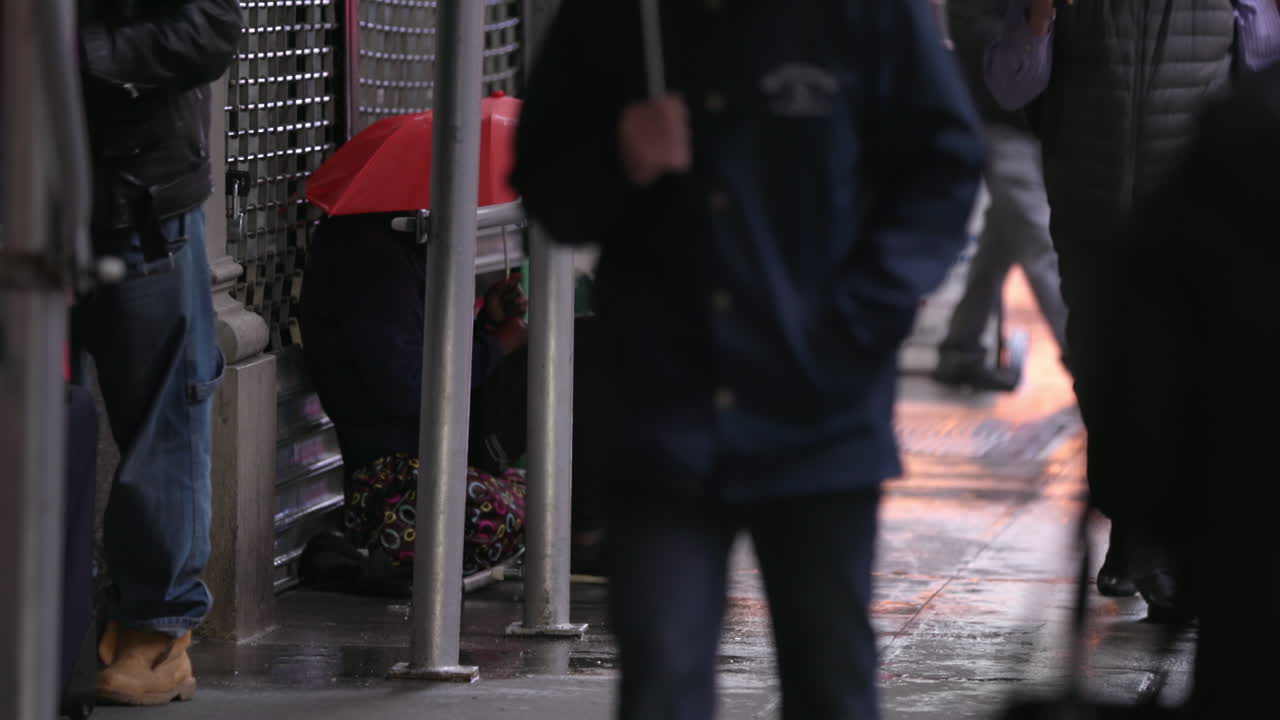 Homeless person in the street. New York City commuters. Wet day, umbrellas. Manhattan NYC. Slow Motion.