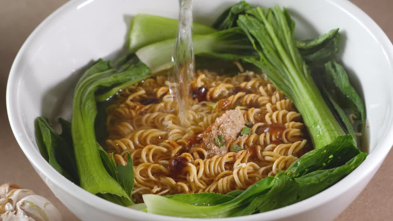 Adding hot water to noodles with bok choy and spices in bowl, Slow Motion