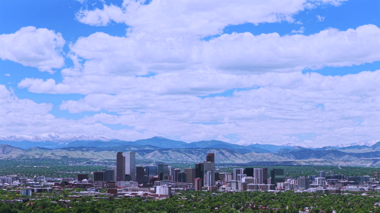 Città di Denver Catena Front Range Montagne Rocciose innevate paesaggio urbano skyline di grattacieli edifici paesaggio centro di Denver Colorado vista aerea con drone primavera quartieri mattina cielo azzurro nuvole cerchio a destra