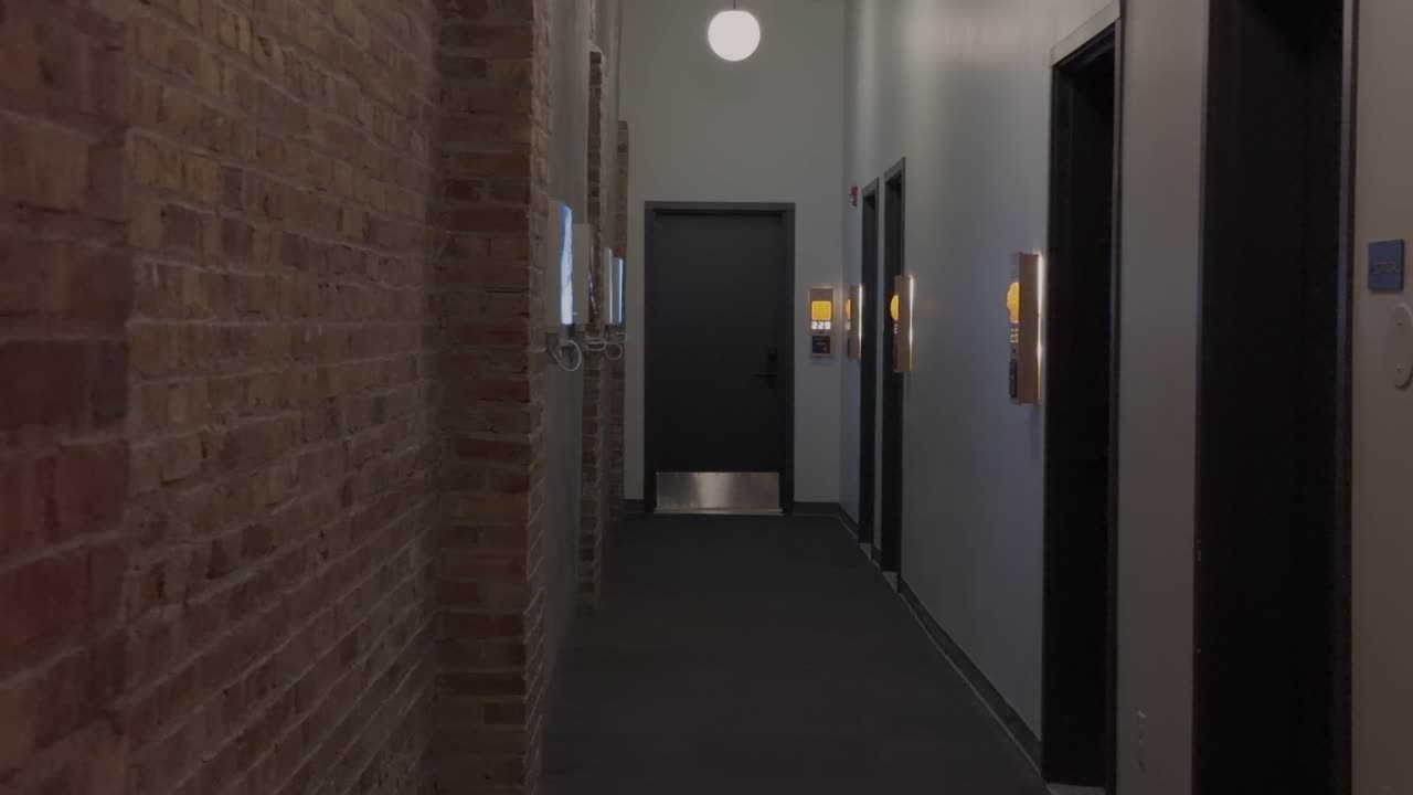 Ripresa a scorrimento lento lungo un corridoio tranquillo con mattoni e illuminazione moderna.