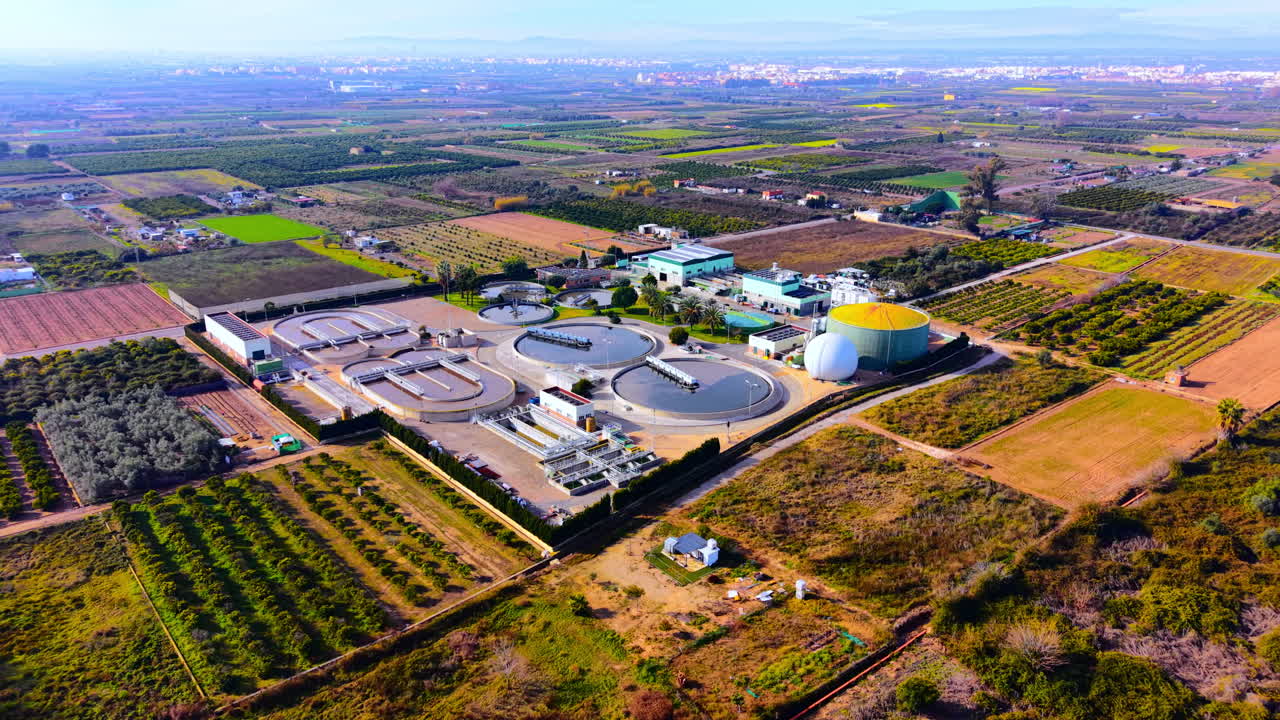 Water reclamation facility with circular tanks surrounded by agricultural fields and orange groves under clear sky. Aerial view of a modern wastewater treatment plant in rural area