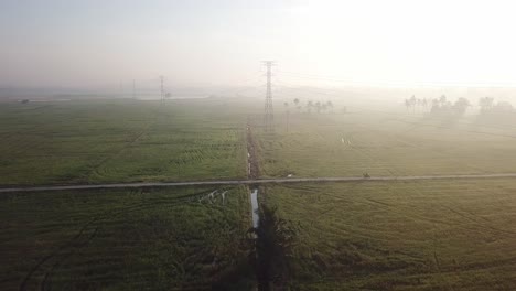 Vuelo-Aéreo-Hacia-El-Motociclista-En-La-Pequeña-Carretera-En-Los-Arrozales.