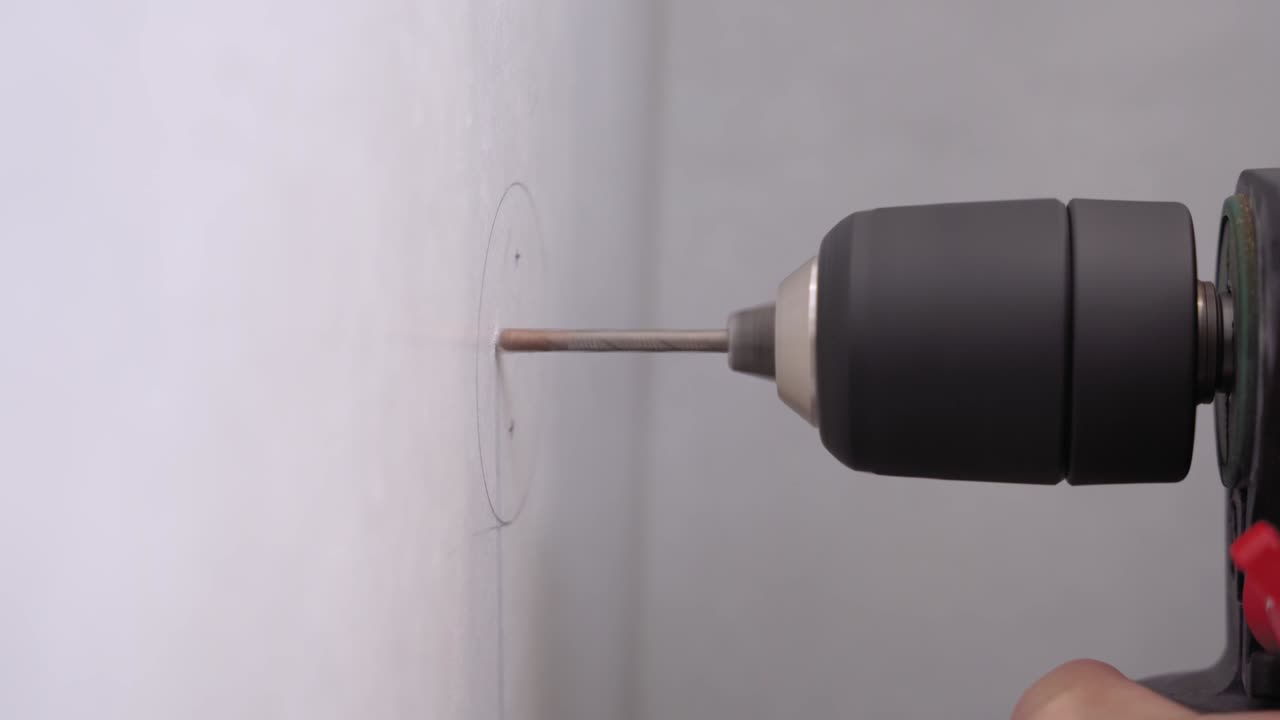 Handyman has drawn circle with pencil and made x marks on the wall. Worker starting to drill holes in surface to insert bolts and hang shelf or hooks, install furniture, close up.