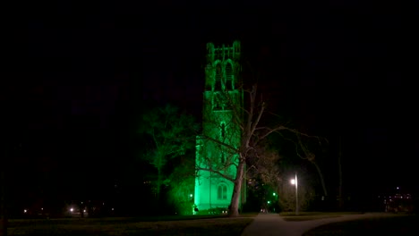 beaumont tower on the campus of michigan state university lit up at night in green in honor of the victims of the february, 2023 mass shooting with wide video walking on sidewalk