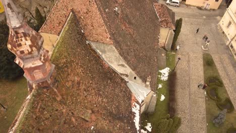 A-approaching-drone-shot,-capturing-the-rooftops-of-a-vintage-locality-in-the-city-of-Sighisoara-on-an-afternoon-with-residual-snow-on-top-of-and-beside-the-buildings-and-a-cityscape-in-the-background