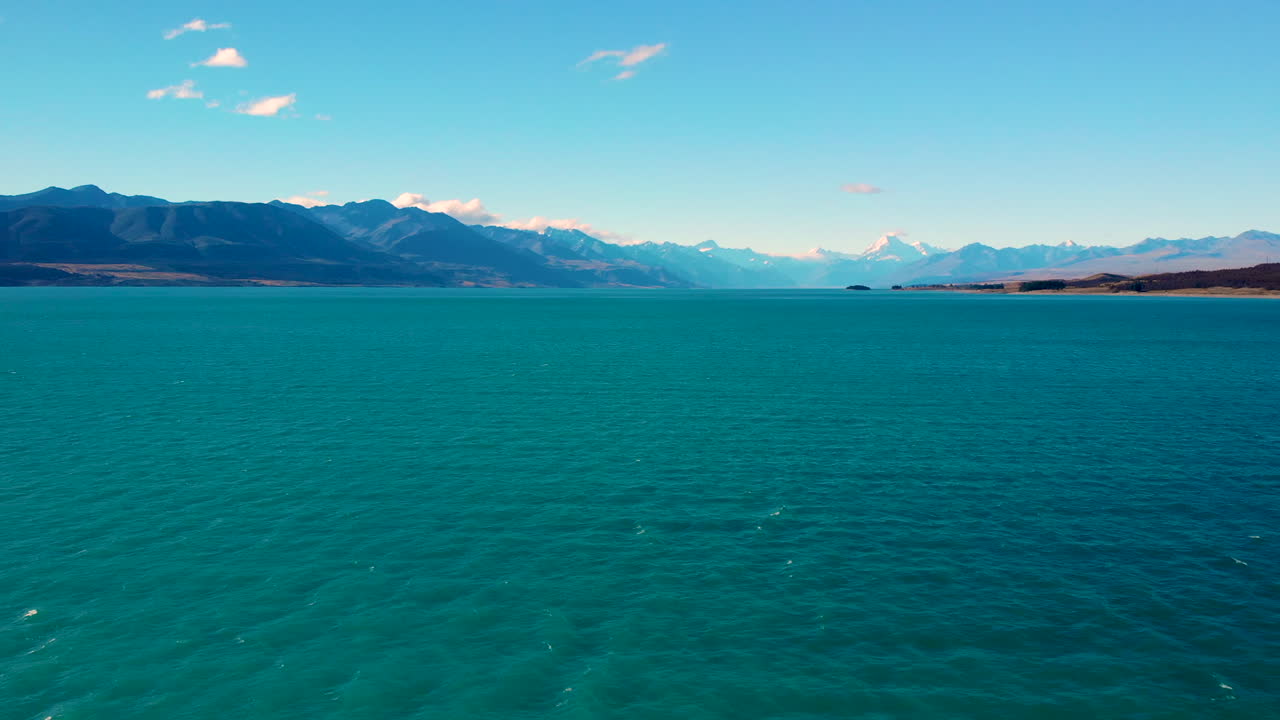retirada aérea por encima de las aguas turquesas del lago pukaki, altas montañas en el horizonte, nueva zelanda