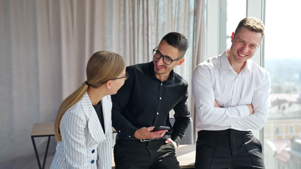Positive cheerful colleagues standing in office discussing something and laughing. People talking and having fun at office during lunch break.