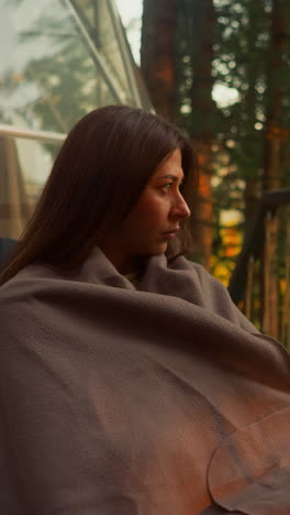 pensive woman covered with soft blanket on balcony watching beauty environment. woman alone looks at sunrise of morning summer sun with sad look