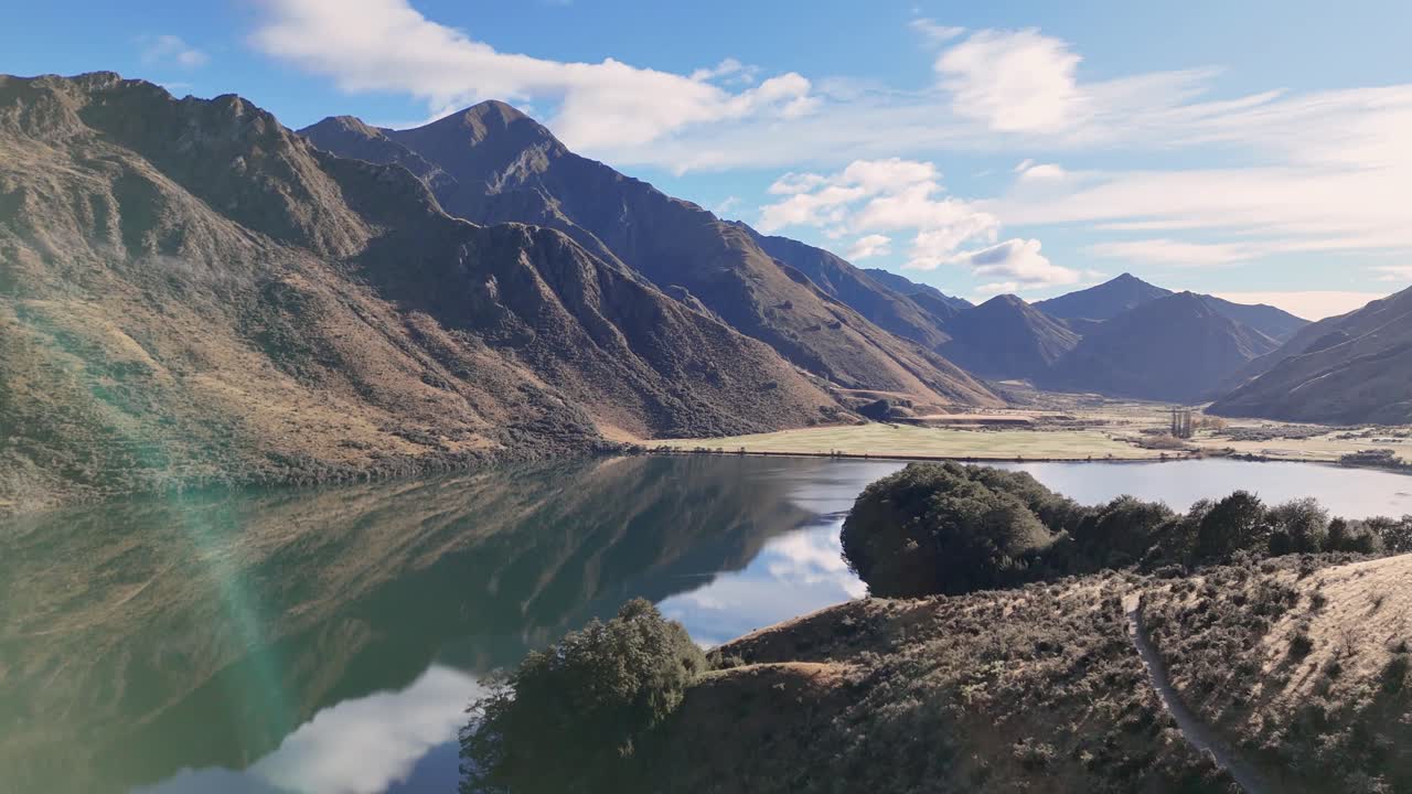 A tranquil view of Lake Moke in Queenstown, New Zealand, with surrounding mountains under clear blue skies and soft natural lighting