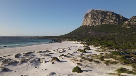 white sandy bay on a clear sky day with a large cliff in the background moonlight beach, pringle bay